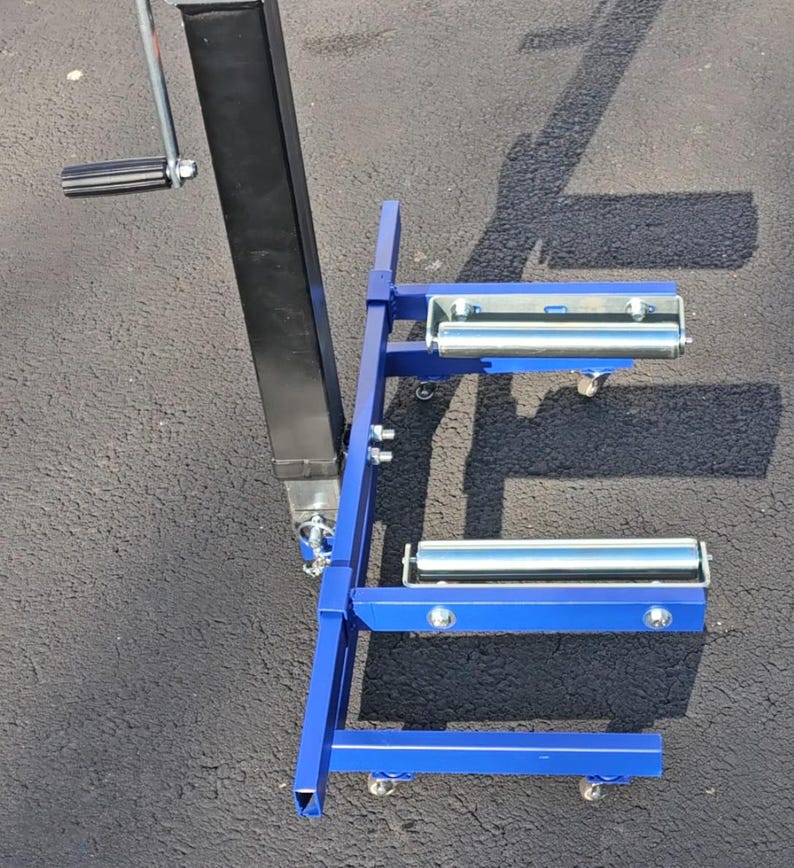 Puede incluir: Soporte de metal azul con cuatro ruedas y dos rodillos. El soporte tiene un poste de metal negro con un asa.