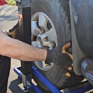 Puede incluir: Un gato de coche de metal azul con un gato hidr&aacute;ulico negro y una rueda encima. El gato tiene dos ruedas a cada lado y una manija para subir y bajar el gato.