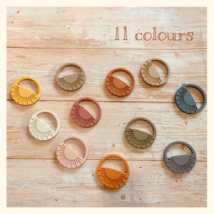 May include: Eleven silicone teethers in various colors, each shaped like a sun with a half-circle design. The teethers are arranged on a light wood surface.