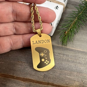 May include: Gold chain necklace with a gold dog tag pendant. The pendant has the name "LANDON" engraved on it and a black silhouette of a video game controller.