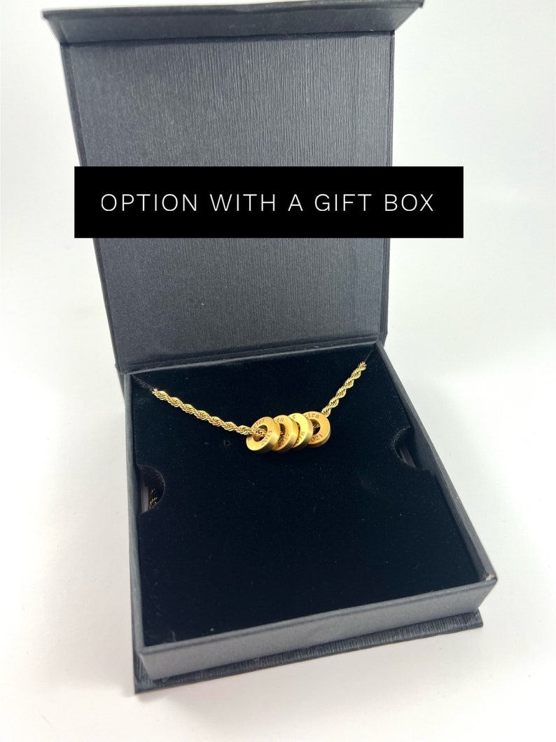 Peut inclure: Un collier en or avec une cha&icirc;ne et cinq breloques rondes dans une bo&icirc;te cadeau noire. La bo&icirc;te porte l'inscription "OPTION WITH A GIFT BOX" sur le dessus.