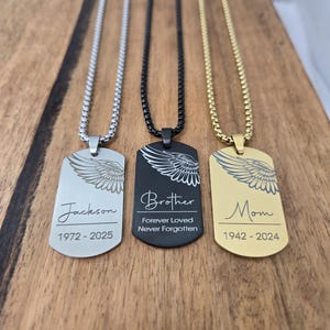 May include: Three dog tag necklaces with ball chains. One is silver with "Jackson" and dates, another is black with "Brother" and "Forever Loved Never Forgotten", and the last is gold with "Mom" and dates. Each tag has a wing design.