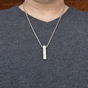 May include: A silver chain necklace with a silver bar pendant engraved with the dates "1923 - 2024".