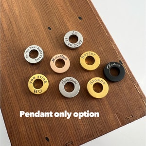 May include: A collection of eight round metal pendants with various engravings. The pendants are arranged on a wooden surface. The engravings include names, dates, and phrases such as "You stink" and "Next Right Turn".