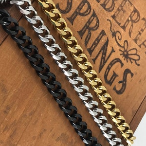 May include: Three curb chains in black, silver, and gold. The chains are laid out on a wooden surface with the text "ALBERT SPRINGS" visible.