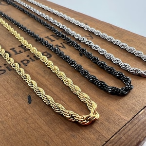 May include: Four different rope chains in gold, silver, black, and silver. The chains are laid out on a wooden surface.
