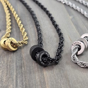 May include: Three necklaces with different chain styles and personalized charms. The gold chain has two charms with the initials "L & L". The black chain has two charms with the words "no matter what". The silver chain has three charms with the name "Keaton".