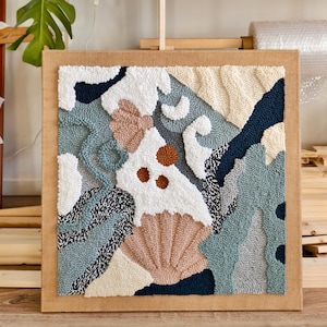 Può includere: Un'opera d'arte da parete quadrata realizzata con la tecnica punch needle, caratterizzata da una composizione astratta di filati testurizzati nei toni del blu navy, verde salvia, crema, bianco e pesca. Include forme organiche e conchiglie.