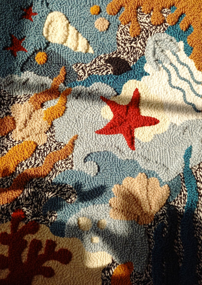 May include: A colorful rug with a blue background and various shapes, including a starfish, seashells, and coral. The rug is made of yarn and has a textured surface.