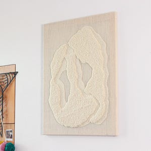 May include: A white textured wall hanging with a raised design of a white abstract shape.