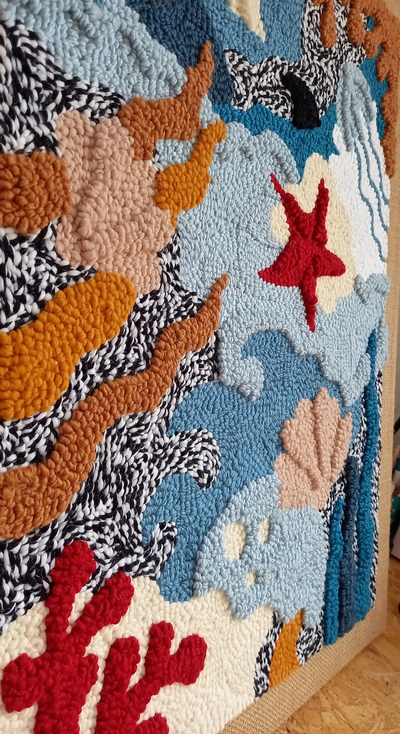 May include: A colorful abstract wall hanging made with yarn and a punch needle technique. The design features a variety of shapes and colors, including blue, red, orange, and white.