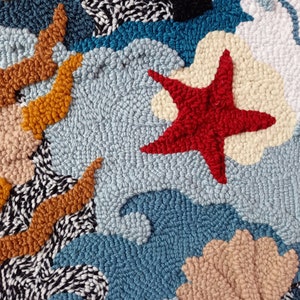 May include: A close-up of a colorful rug with a red starfish, blue waves, and a tan seashell. The rug is made of yarn and has a textured surface.
