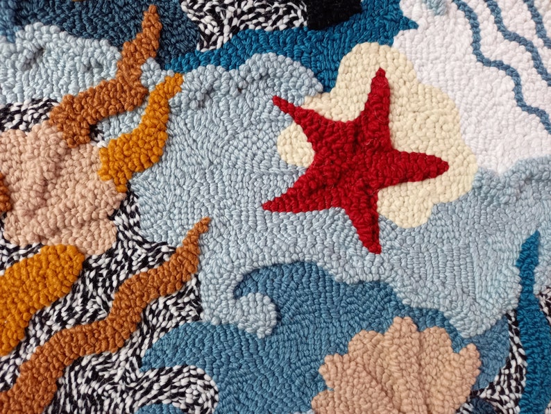 May include: A close-up of a colorful rug with a red starfish, blue waves, and a tan seashell. The rug is made of yarn and has a textured surface.