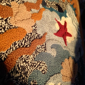 May include: A close-up of a colorful, textured wall hanging with a variety of shapes and patterns. The wall hanging is made of yarn and features a red starfish in the center.