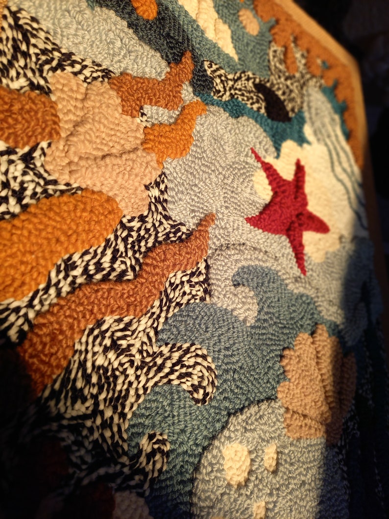 May include: A close-up of a colorful, textured wall hanging with a variety of shapes and patterns. The wall hanging is made of yarn and features a red starfish in the center.