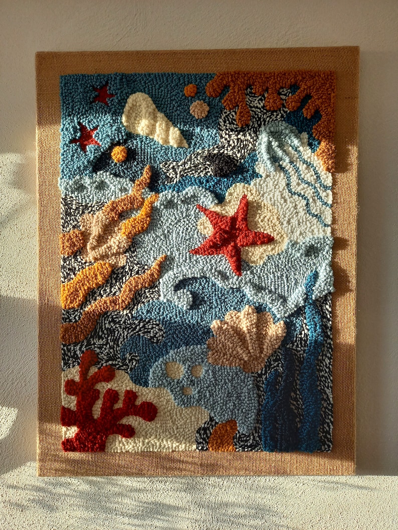 May include: A colorful abstract wall hanging with a blue background and various shapes and textures, including seashells, starfish, and coral. The wall hanging is made of yarn and is framed with a burlap border.