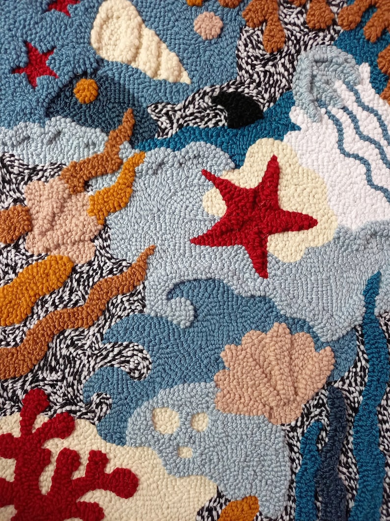 May include: A colorful rug with a variety of textures and shapes, including seashells, starfish, and coral. The rug is made of yarn and has a blue background.