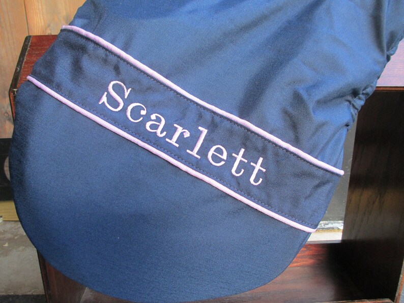 May include: A navy blue saddle pad with a pink trim and the name "Scarlett" embroidered in white.