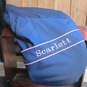 May include: A navy blue saddle pad with a white embroidered name "Scarlett" in a lavender coloured border.