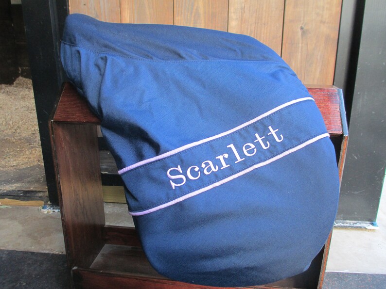 May include: A navy blue saddle pad with a white embroidered name "Scarlett" in a lavender coloured border.