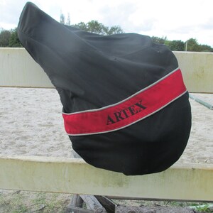 May include: Black saddle cover with a red and grey trim. The cover has the word "ARTEX" embroidered on it.