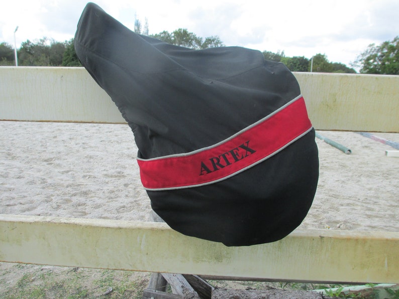 May include: Black saddle cover with a red and grey trim. The cover has the word "ARTEX" embroidered on it.