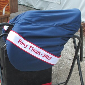 May include: A blue saddle cover with a white and red ribbon that says "Pony Finals-2015".