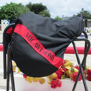 May include: Black saddle cover with a red stripe and the text "MR. AWESOME" embroidered in black.