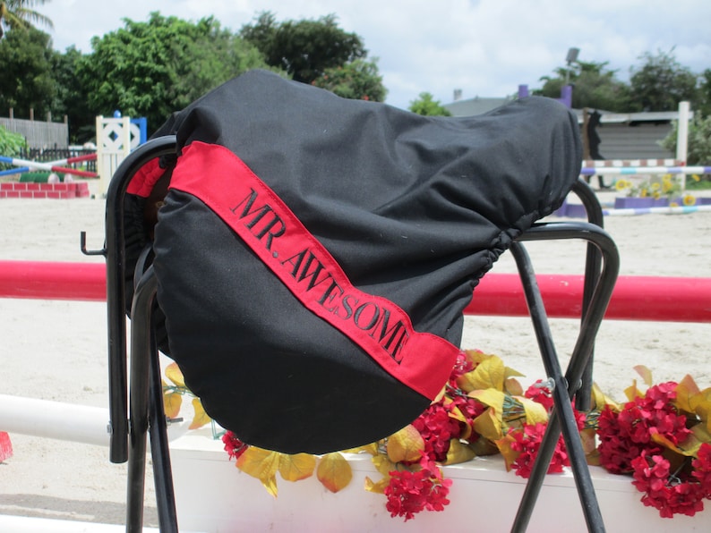 May include: Black saddle cover with a red stripe and the text "MR. AWESOME" embroidered in black.
