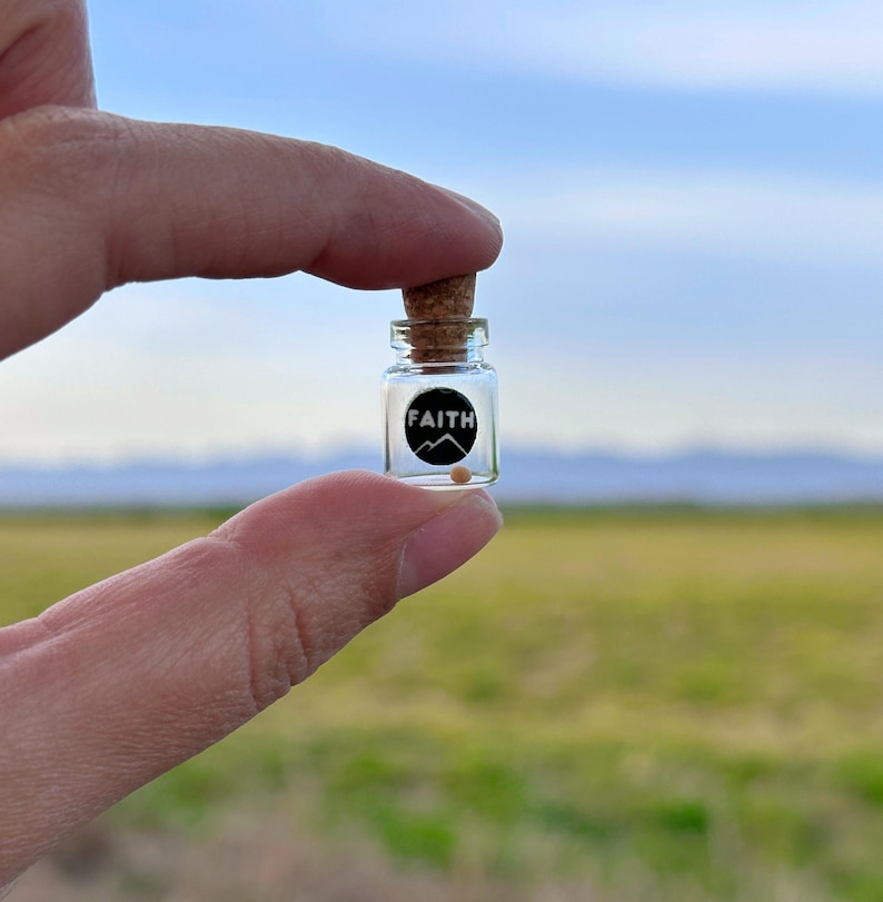 May include: A small glass bottle with a cork stopper, containing a single bead. The bottle has a black and white label with the word "FAITH" and a mountain graphic.