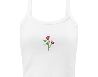 Puede incluir: Un top corto blanco sin mangas con un pequeño bordado centrado de un tallo verde con dos flores rosas. La prenda tiene un cuello redondo y tirantes anchos, ofreciendo un aspecto sencillo y limpio para este artículo de ropa.