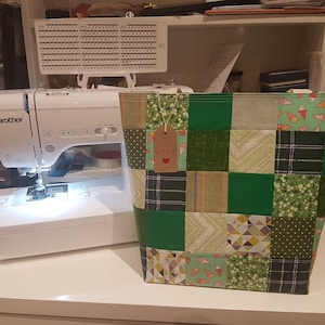 May include: A green and white patchwork tote bag with a brown tag that says "Love" on it. The bag is sitting on a white table next to a white sewing machine.