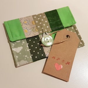 May include: A green and brown patchwork fabric purse with a button fastening and a brown paper tag that says "A.P.O.K." with a red heart.