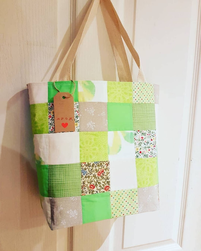 May include: A green patchwork tote bag with a brown tag that says "A.P.O.K." in red lettering. The bag has a variety of green, white, and brown patterned fabrics.