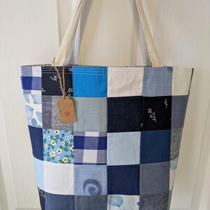 May include: A patchwork tote bag made from blue and white fabric scraps. The bag has a cream-colored canvas strap and a small brown tag with the word "Love" on it.