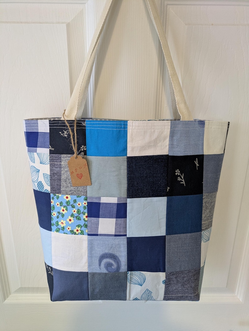 May include: A patchwork tote bag made from blue and white fabric scraps. The bag has a cream-colored canvas strap and a small brown tag with the word "Love" on it.