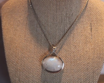 Puede incluir: Un collar de cadena de plata con un colgante redondo de piedra de luna blanca.