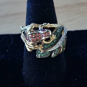May include: A gold ring with a green and red gemstone design. The ring features a stylized frog design with green and red gemstones set in gold.