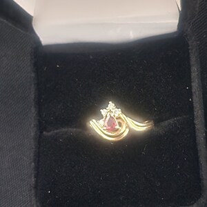 May include: A gold ring with a red gemstone and small diamonds set in a wave-like design.