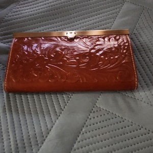 May include: A brown leather wallet with an embossed floral design and a gold metal clasp.