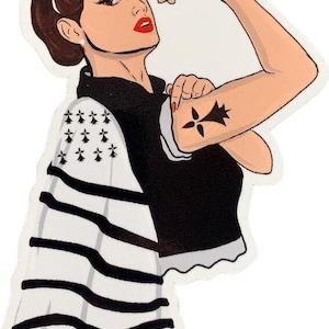 Peut inclure: Une illustration en noir et blanc d'une femme aux cheveux bruns portant une chemise à rayures noires et blanches et une écharpe blanche avec un motif de drapeau breton noir. Elle fléchit son biceps et a un tatouage noir d'une fleur de lys sur son bras.