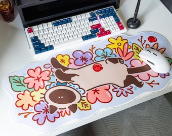 May include: A white mousepad with a cartoon cat sleeping in a bed of colorful flowers. The cat is brown and white with a pink nose. The flowers are pink, purple, yellow, and green. There is a white computer mouse on the mousepad.