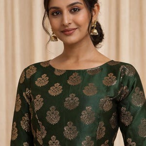 May include: A dark green blouse with a gold floral pattern. The blouse has a round neckline and short sleeves. The model is wearing gold earrings.