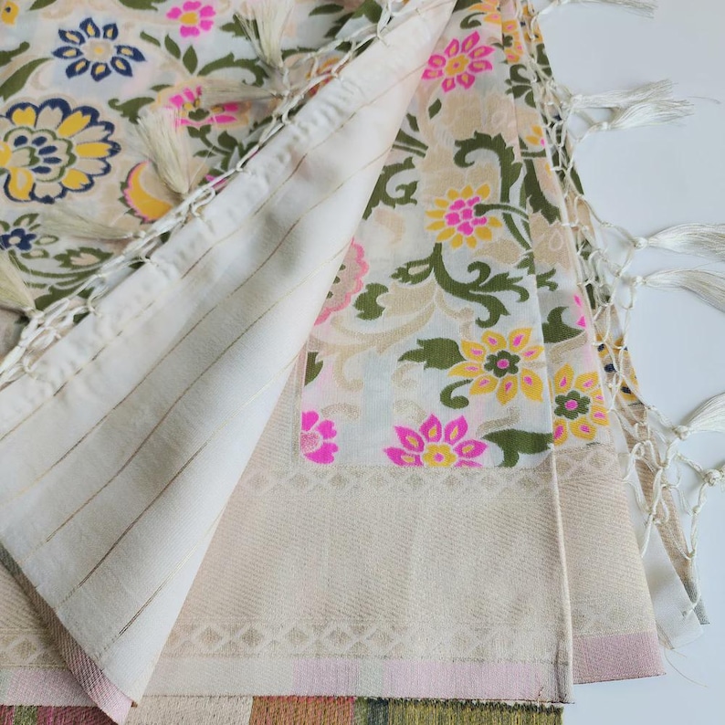 May include: Cream-colored textile with a floral pattern in pink, yellow, and green. The fabric has a striped section and is trimmed with tassels. The design features a repeating floral motif, creating a decorative and elegant look.