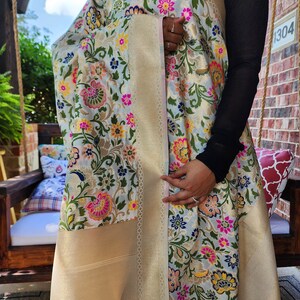 May include: A light blue and gold floral shawl with a detailed border. The shawl features a repeating pattern of colorful flowers in pink, yellow, and blue. The border is a solid gold color.
