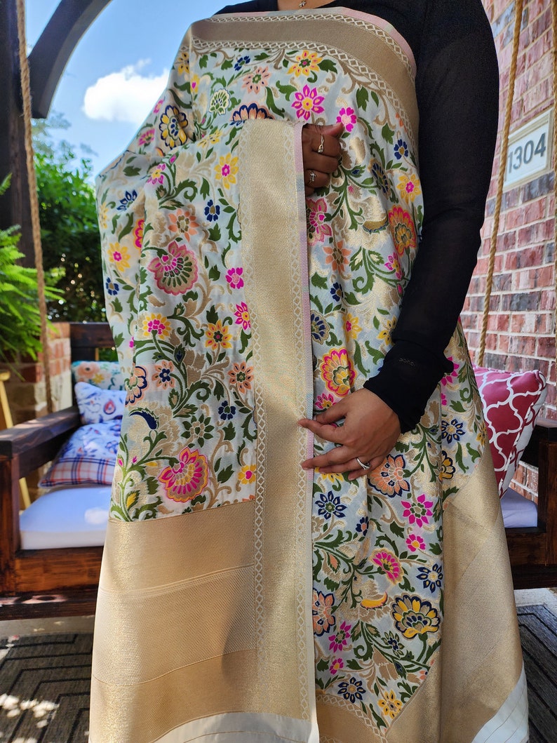 May include: A light blue and gold floral shawl with a detailed border. The shawl features a repeating pattern of colorful flowers in pink, yellow, and blue. The border is a solid gold color.