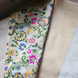 May include: Close-up of a folded fabric with a floral pattern. The fabric features a light blue background with colorful flowers in pink, yellow, and blue, and green leaves. The fabric on the right is a solid beige color with a subtle pattern.