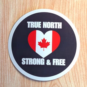 May include: A round black and white sticker with the text "TRUE NORTH" and "STRONG & FREE" in white. A red maple leaf is inside a white heart with red and white stripes, representing the Canadian flag.
