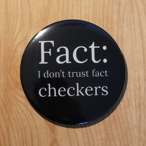 Può includere: Un bottone nero con testo bianco che dice "Fact: I don't trust fact checkers".