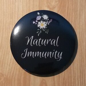 May include: A black round button with a white floral design and the text "Natural Immunity" in white.